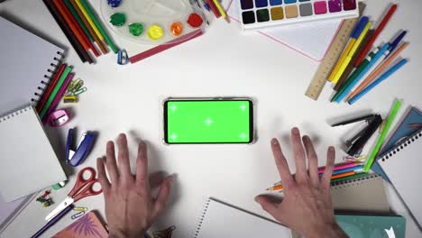 top view of man hands knocking by fingers on table full of school accessories in front of a mobile