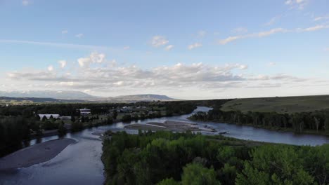 Toma-De-Ariel-De-Un-Pequeño-Pueblo,-Un-Río-Y-Las-Montañas-En-La-Distancia