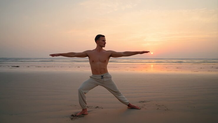 Uomo che pratica la posizione del guerriero yoga su una spiaggia al tramonto