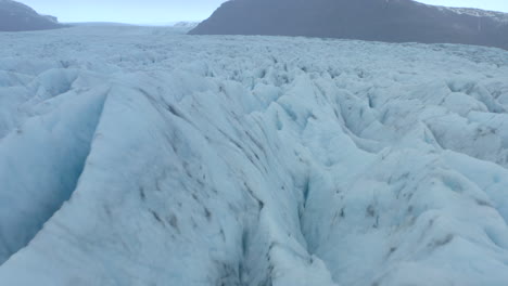 low cinematic aerial shot over cracks and ridges in a large glacier