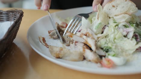 mujer joven comiendo una ensalada fresca en una mesa de madera en un restaurante moderno con grandes ventanas, luz natural y vistas urbanas. escena de comedor relajada