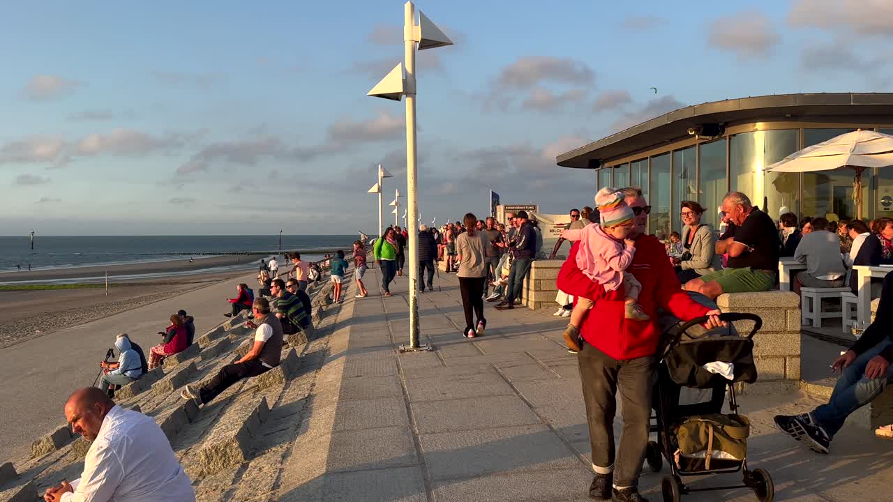 Pov walk of enjoying people along promenade on Norderney Island, Germany. Beautiful sunset time. SLow motion.