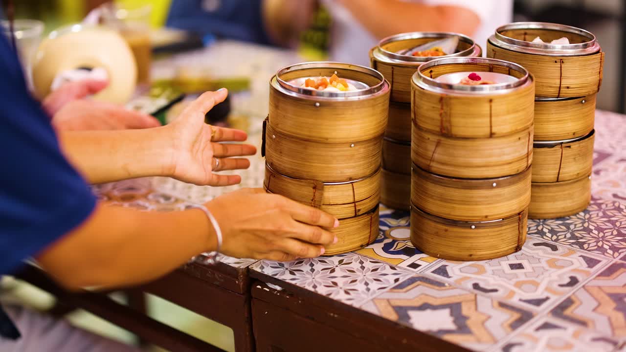 A lively dining scene with people enjoying dim sum at a patterned table in Phuket, Thailand. Warm lighting enhances the inviting atmosphere