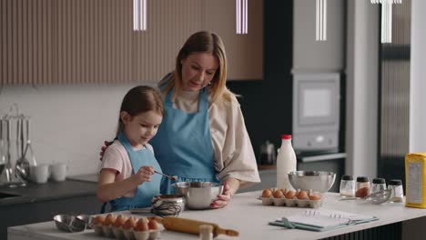 cute child girl is helping to her mother in kitchen, mom and daughter are cooking together