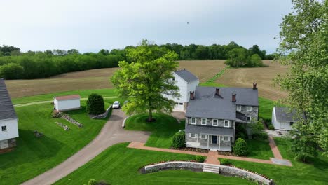 aerial view of a peaceful countryside estate with a farmhouse, barn, lush green lawn, large trees, and open fields under a clear sky. american farmland in usa.