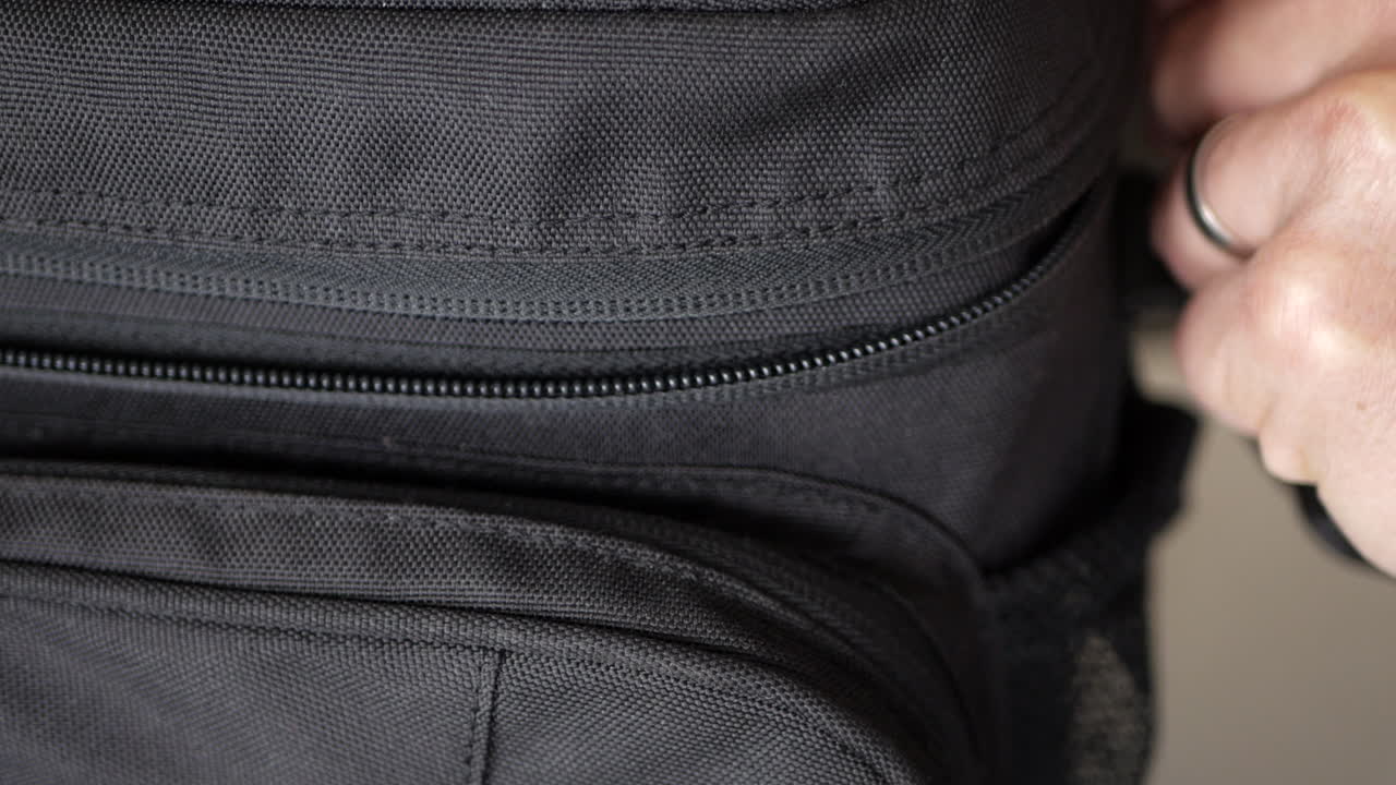 백인 남성이 지퍼를 닫고 있는 검은색 카메라 가방