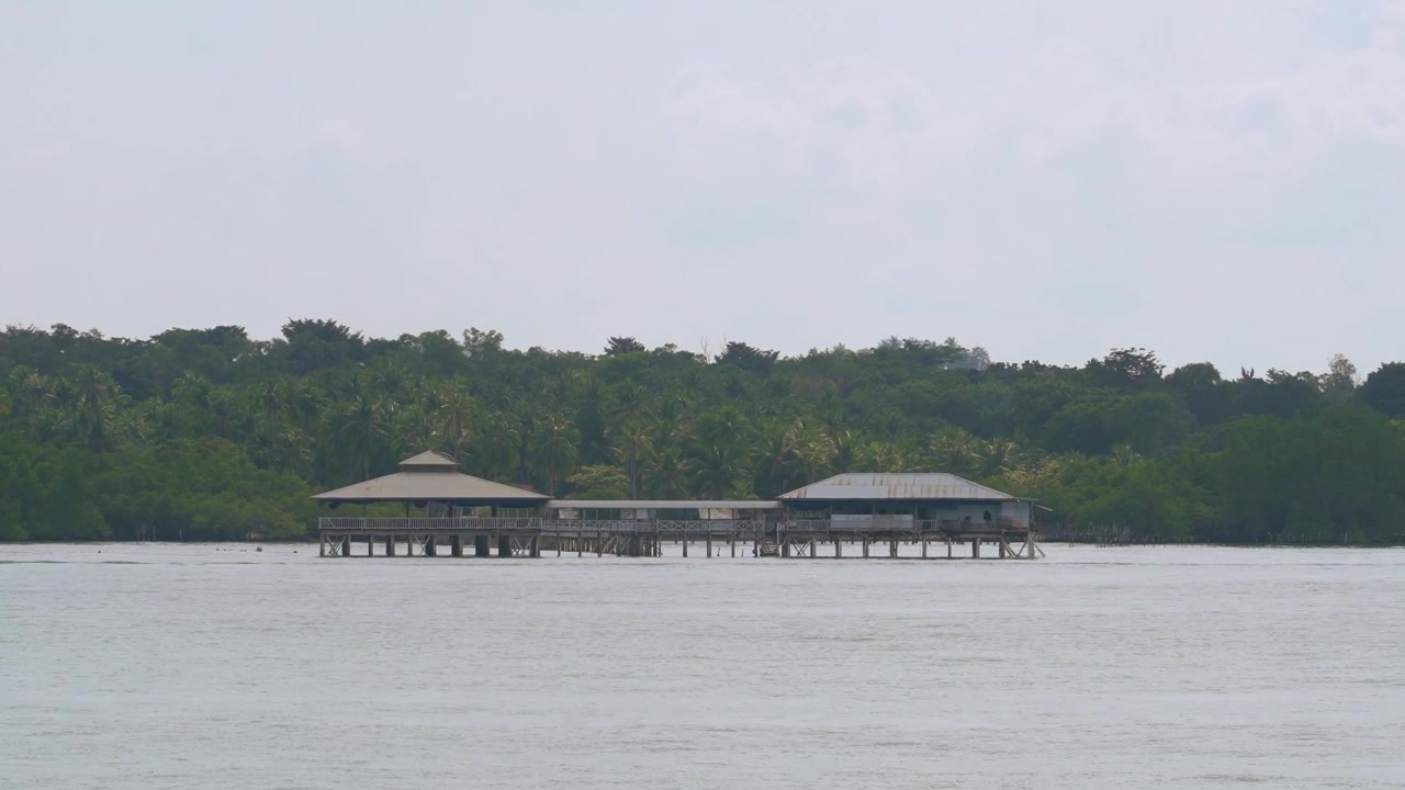 Una veduta cinematografica di tradizionali case su palafitte e passerelle in legno costruite su acque calme con uno sfondo di lussureggiante foresta tropicale nel Sud-est asiatico. Ideale per temi di viaggio, cultura e stile di vita costiero.