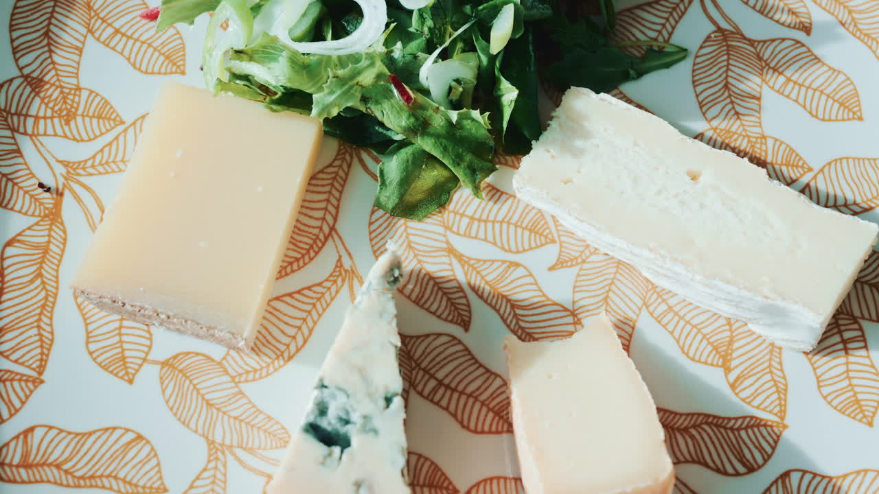 Close up of a cheese plate with assorted cheeses and salad on an elegant patterned plate