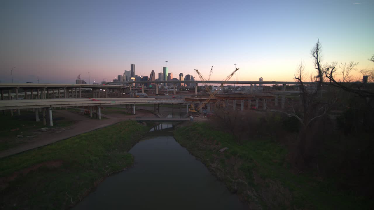 Un'ampia ripresa aerea che cattura la grandezza di Houston mentre il drone sale, svelando l'intricata struttura di un enorme svincolo autostradale contro i caldi toni dorati di un sole al tramonto.