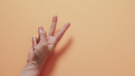 Close-up-of-hand-of-cacausian-woman-showing-peace-sign-with-copy-space-on-yellow-background