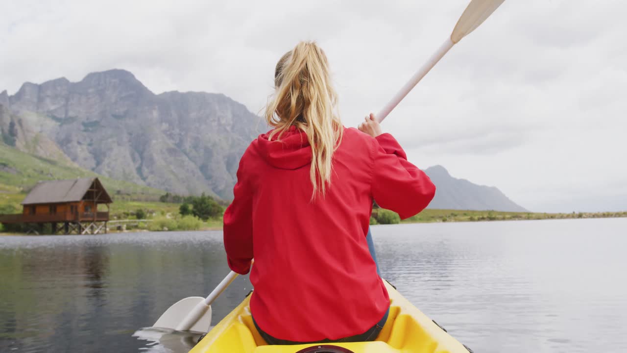 Caucasian woman having a good time on a trip to the mountains, kayaking on a lake, holding a paddle,