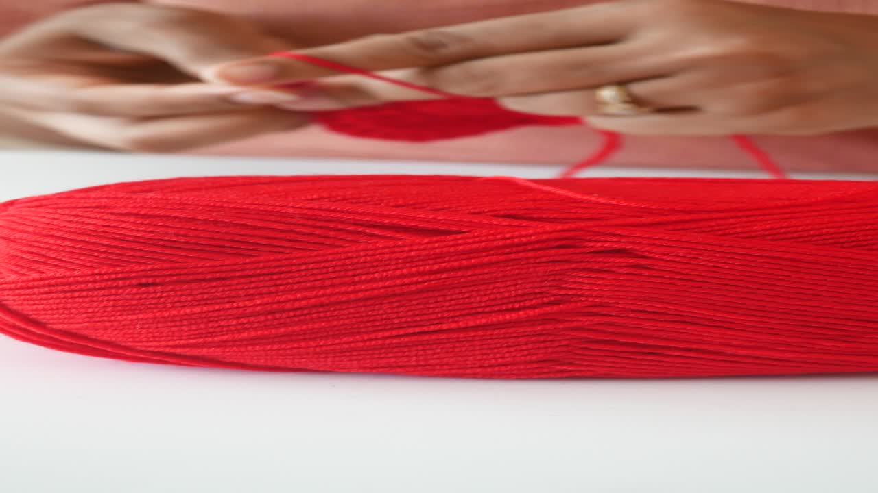 primer plano de las manos de una mujer tejiendo con hilo rojo
