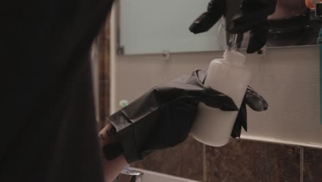 a person with black hand gloves thoroughly put hair bleach powder into the bottle container for mixing and application in toronto canada - close up shot