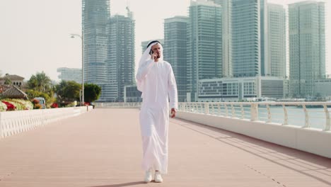 man in traditional attire walking and talking on phone in dubai