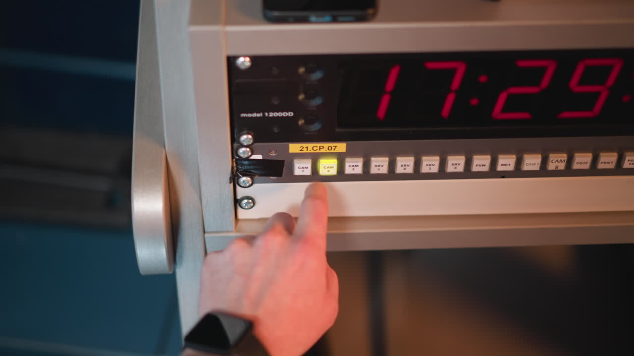 Close-up shot of hand pressing a button on a control panel with a bright green light and timer display in studio setting. Technology equipment for video production in action
