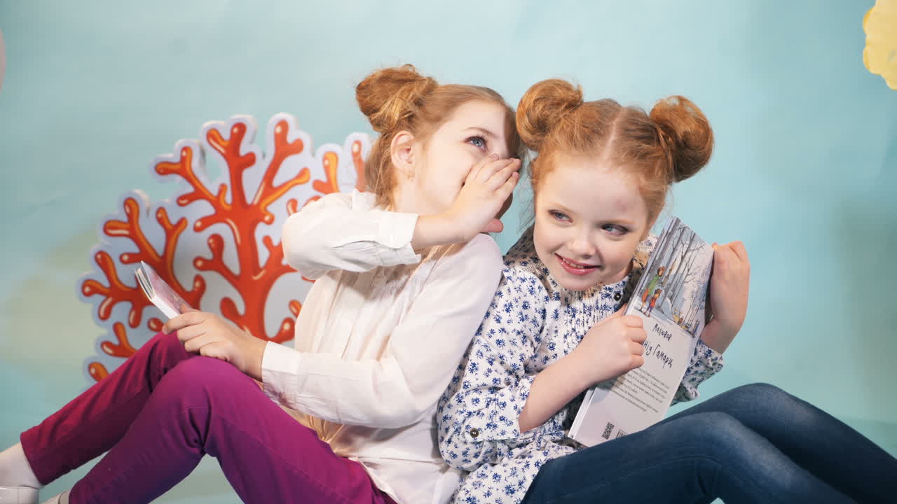 Two little girls reading a book on a blue background. Friends. Childhood. Friendship. Fairy Tales.
