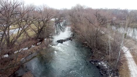 small river dam and rapids on scenic, idyllic, willow tree lined flowing river in winter in rural countryside in boise, idaho, usa