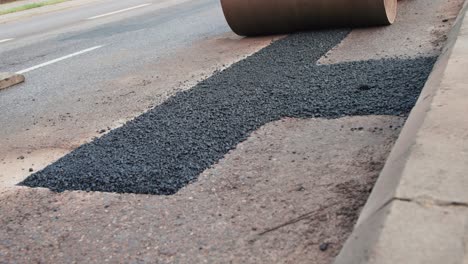 close up view of freshly patched up road with hot asphalt driven over by compactor