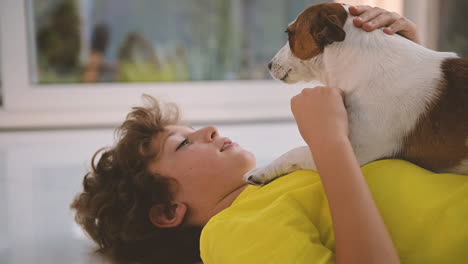 side view of a blond boy with curly hair lying on the floor and caresses his dog 1