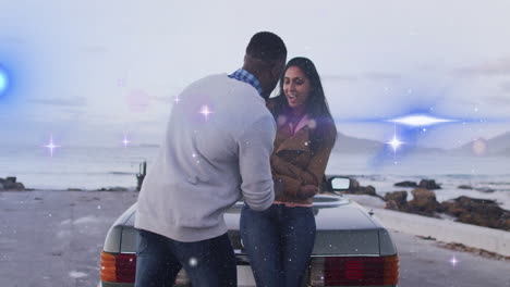 man kneeling before woman sitting on rocky beach near convertible, showing ring box for wedding ads
