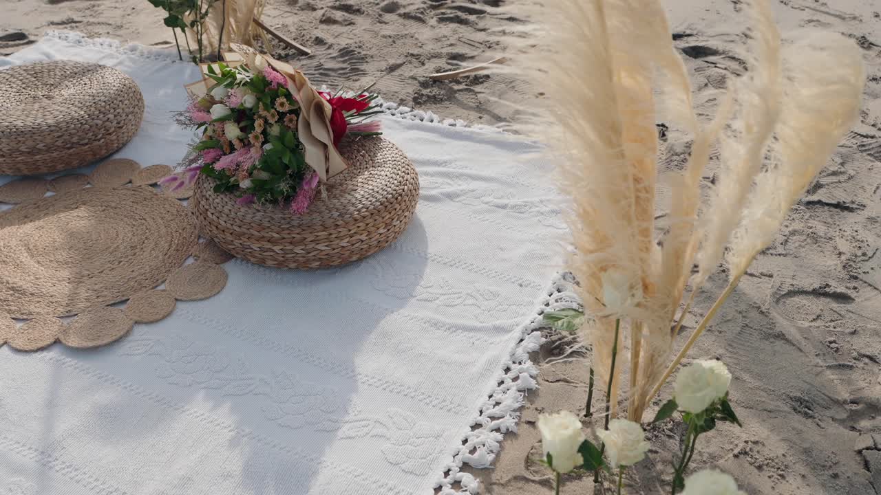 woven cushions and flowers on a soft white blanket set on the beach for an intimate moment
