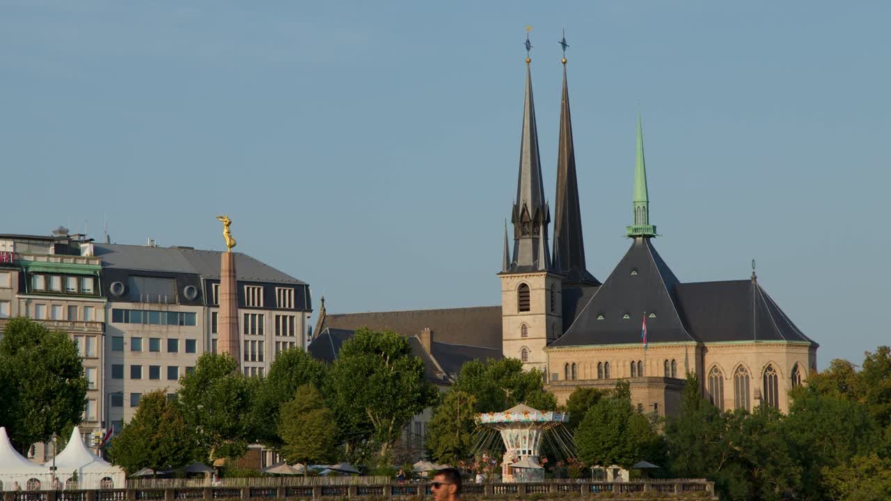 Wide shot of cathedral spires, gold statue, and city buildings in warm sunset lighting