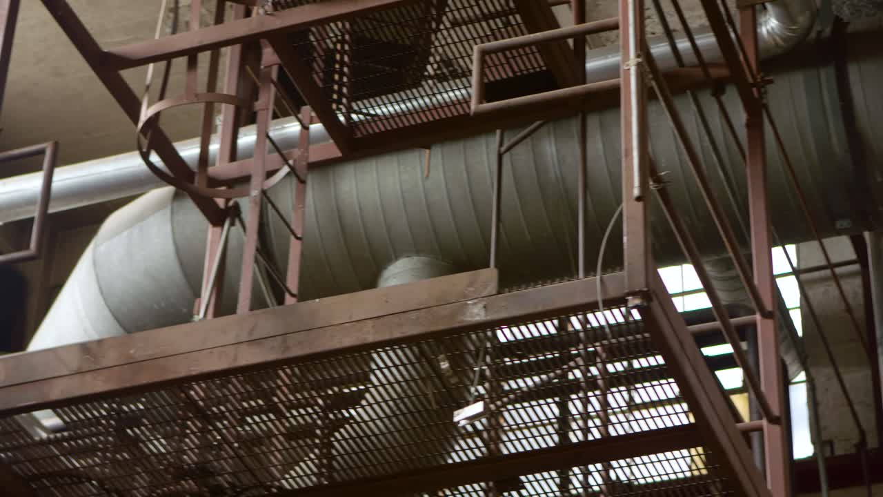 A pan shot of a large air duct on the ceiling of an abandoned factory