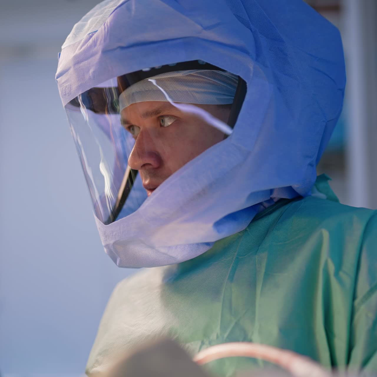 Mid-aged Caucasian male surgeon in protective helmet listens to his colleague. Portrait of a focused medic at surgery