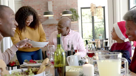 happy african american mother serving dish to multi generation family at christmas dinner table