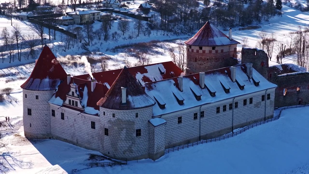 Orbita aerea con parallasse intorno al Castello medievale di Bauska con tetti di tegole rosse e torri coperte di neve in una soleggiata giornata invernale in Lettonia.