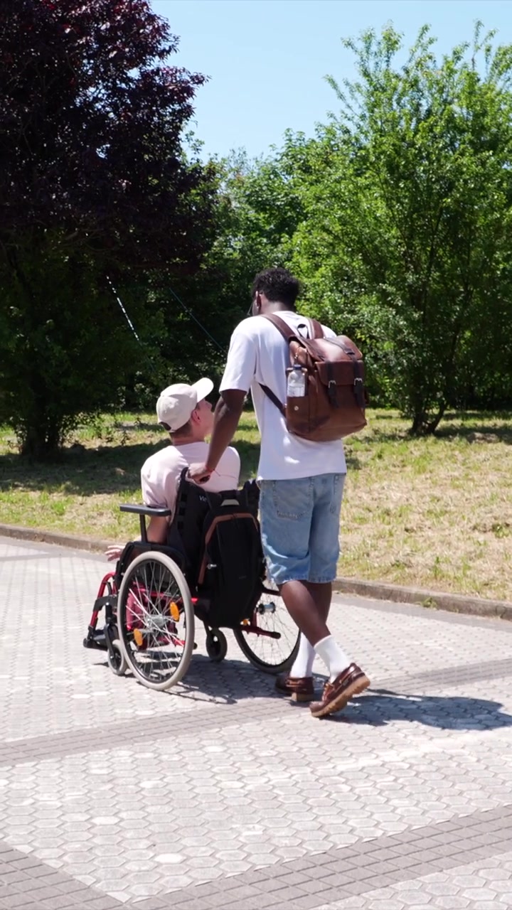 Giovane uomo che spinge un amico su sedia a rotelle attraverso il parco