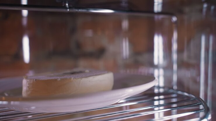 Creamy dessert cake with smooth frosting placed on white plate, rotating on metal shelf inside transparent display fridge under soft lighting, highlighting texture and chilled presentation