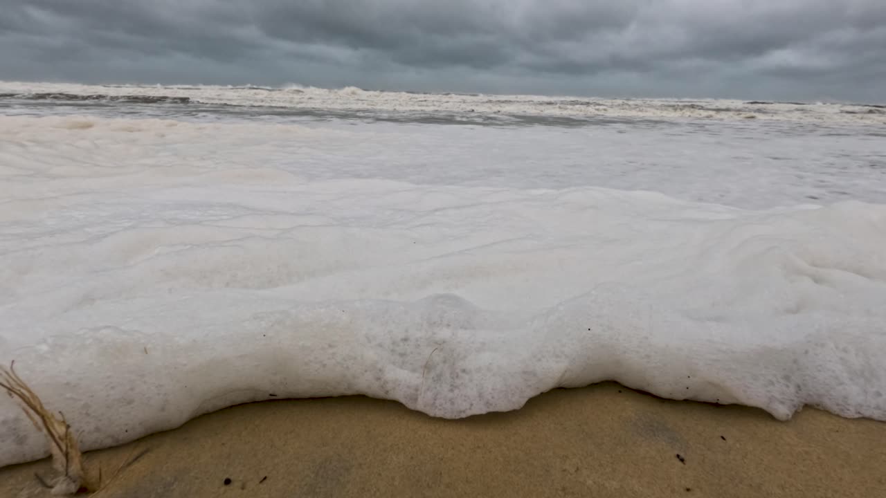 은 파도가 구름이 가득한 하늘 아래의 모래 해변에 부히며 폭풍우를 일으키는 바다 사이클론 알프레드의 힘과 움직임을 포착합니다.