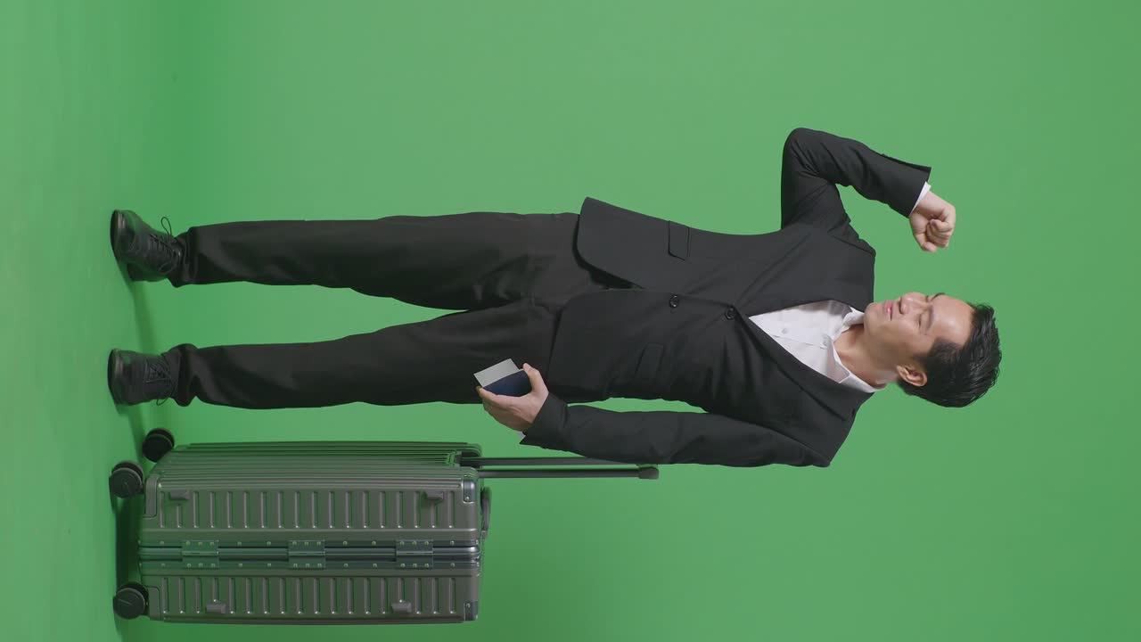 가방과 여권으로 가득 찬 아시아 사업가 여행자가 녹색 스크린 배경 스튜디오에 서있는 동안 미소 짓고 팔꿈치를 구부리고 있습니다.