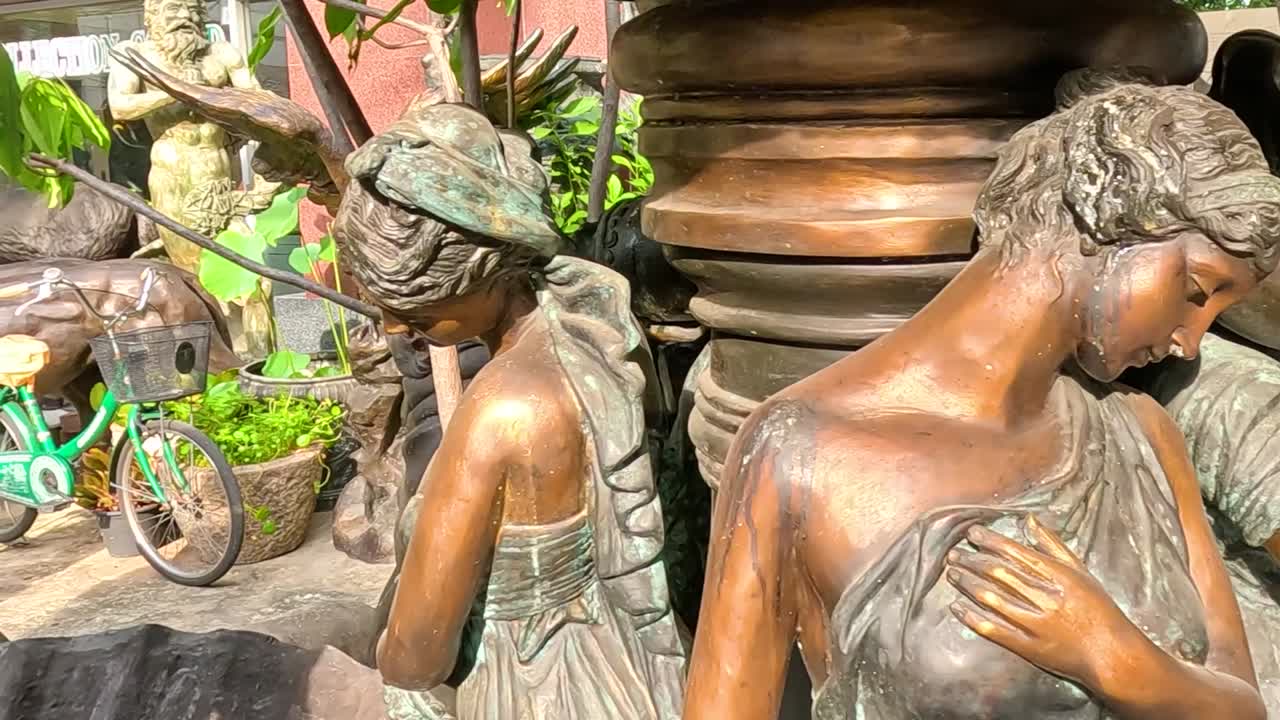 Cropped view of bronze statues surrounded by lush greenery in an outdoor setting.