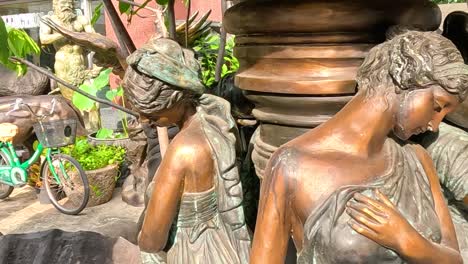 cropped view of bronze statues surrounded by lush greenery in an outdoor setting.