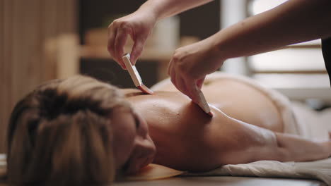 woman is resting in spa-salon lying in massage parlor masseur is stroking female back by brush with oil