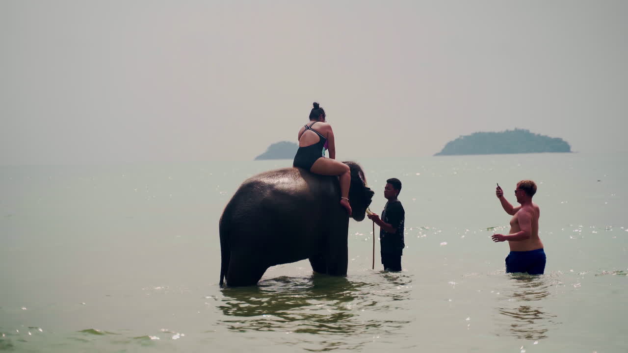 Tourists riding elephant and taking pictures in sea water, Thailand.