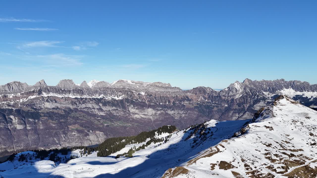 En majestætisk vinterpanoramaudsigt over de schweiziske alper. Klar, blå himmel over de sneklædte skråninger i Flumserberg med de ikoniske, takkede tinder af Churfirsten, der tårner sig op over Flums-dalen og Walensee.