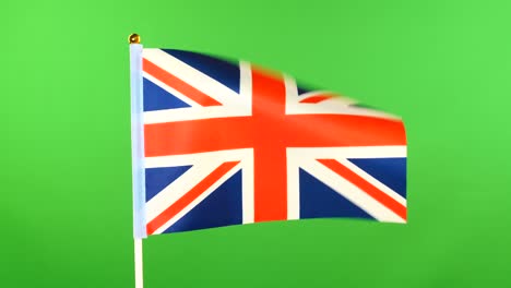 la bandera de gran bretaña en el mástil sobre un fondo verde. la bandera británica ondeando en el viento.