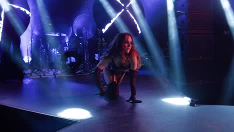 on stage, a girl dances lying down and on her knees under concert lighting