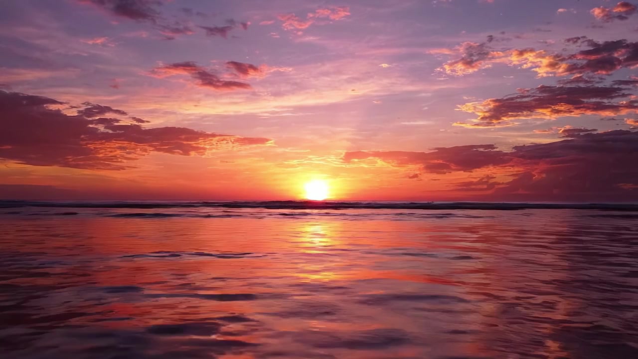 A breathtaking sunset paints the sky in vibrant hues of orange, pink, and purple, reflected in the calm ocean waters at the end of a beautiful day.