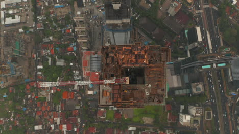 Aerial-tilting-shot-into-overhead-of-tall-modern-skyscraper-under-construction-with-hole-in-the-center-of-the-building