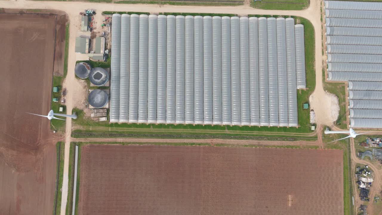Drone Footage Over English Rural Farmland Showing Polytunnels, Wind Turbines, and Scenic Fields in Renewable Energy Landscape