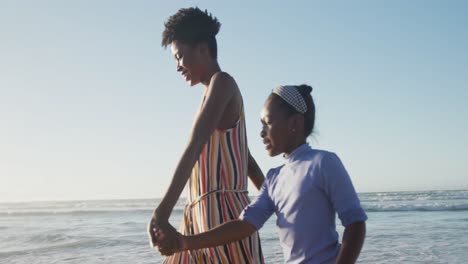 happy african american mother walking with daughter on sunny beach