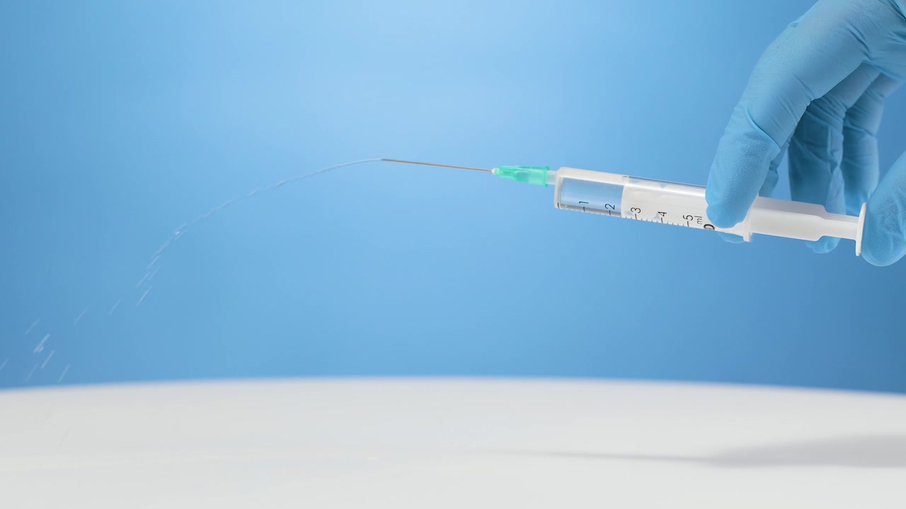 Hand in glove squeezing liquid medication out of medical syringe