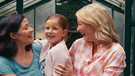 Portrait-Of-Same-Sex-Family-With-Two-Mature-Mums-Hugging-Daughter-As-They-Garden-In-Greenhouse