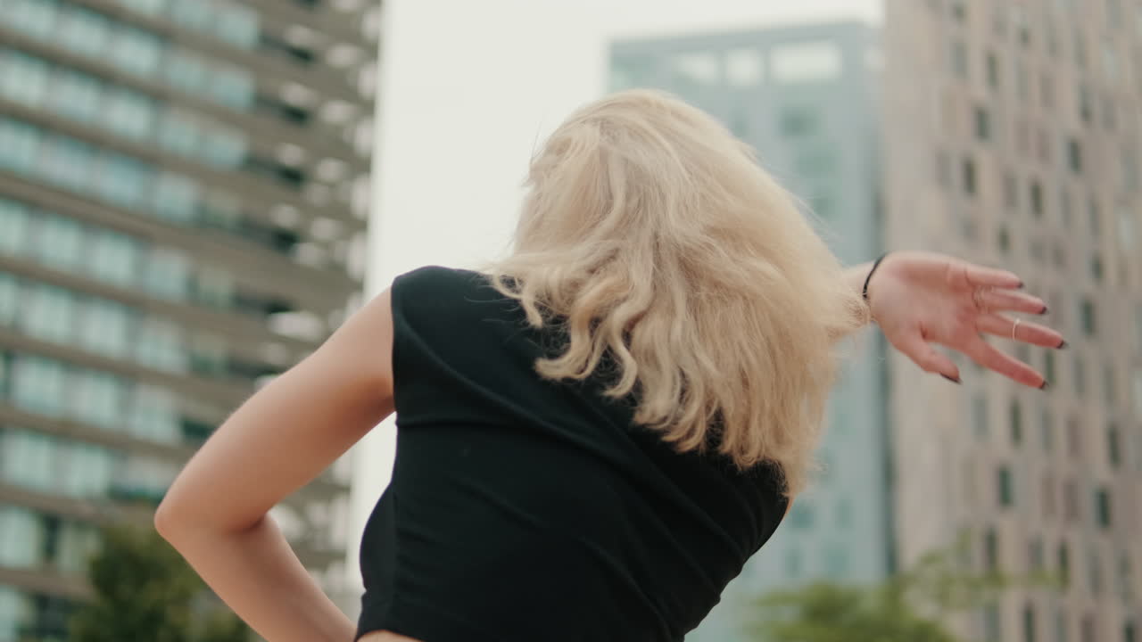 ブロンドの髪の女性が、街の建物を背景にポーズをとっています。