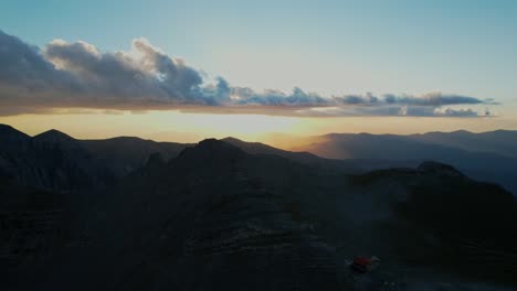 breathtaking sunset from a drone shot going backwards on a high altitude revealing the mountain horizon and a refuge for hikers and climbers