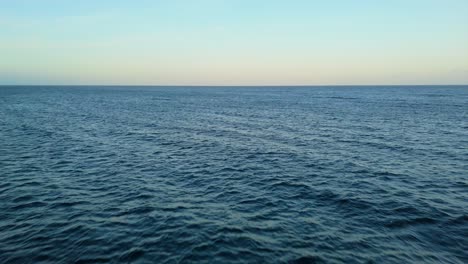 aerial pullback with dark blue water and orange red glow on horizon of the ocean